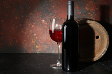 Wooden barrel, bottle and glass of red wine on black table against grunge brown background