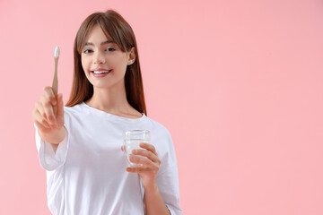 Wall Mural - Beautiful young woman with toothbrush and glass of water on pink background