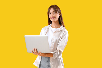 Poster - Beautiful young woman using laptop on yellow background