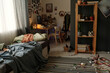 © pressmaster - Spacious messy bedroom with striped rug on the floor, bed with creased sheets and other stuff by window and workplace in the corner