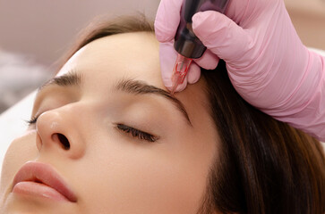 Young woman getting eyebrow permanent makeup in beauty salon.