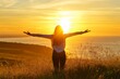 © 为轩 张 - Woman with arms outstretched on a grassy hill, basking in the warm golden light of a beautiful sunrise over the ocean, embodying happiness and peace.
