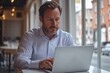 © Tada - man working on laptop business casual attire is focused on typing at his laptop, with an open window behind him overlooking the street outside. He is sitting alone and appears to be working or study