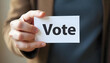 © Aksaka - A Person Holding a White Card with the Word 'Vote' Written on It in Bold Black Letters