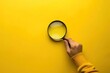 © Tasnim - Hand holding a magnifying glass on a yellow background. Search and investigation concept.