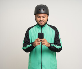 Young asian rider wearing green jacket uniform and bike helmet standing holding smartphone food application on isolated. Male delivery service worker. Delivery courier and shipping food service.