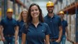 © kotlyarn - A group of warehouse workers in blue uniforms and yellow helmets smile and pose for a photo. The team stands in an industrial warehouse setting surrounded by boxes and equipment.