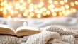 © tashechka - A warm drink steams beside an open book on a soft blanket, surrounded by glowing lights on a chilly winter evening