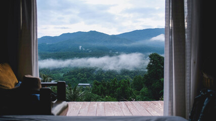 Greenery mountain view on foggy day outside wooden bedroom