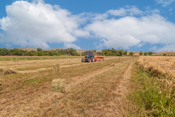 The tractor uses a trailed baling machine to collect straw in the field and form large bales. Agricultural work, baling, baler, hay harvesting in the summer field