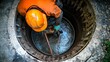 © Dina - worker lowers equipment into a manhole to inspect or repair the underground sewage system