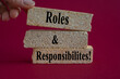 © Liudmila - Roles and Responsibilities symbol. Concept words Roles and Responsibilities on brick blocks on a beautiful pink background. Businessman hand. Business concept.