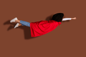 Wall Mural - Full body portrait of nice young girl superhero costume fly isolated on brown color background