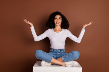 Poster - Full body portrait of nice young girl sit podium hold empty space isolated on brown color background