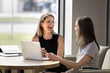 © fizkes - Happy joyful business colleagues sharing laptop at table, talking, discussing work tasks together. Two young businesswomen meeting, chatting, laughing, enjoying teamwork, cooperation, networking