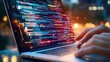 © bteeranan - A person types on a laptop, displaying colorful code and software development in a vibrant nighttime setting.