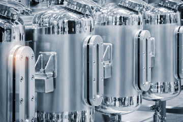 Poster - Three large silver tanks with a bright orange light shining on the middle one. The tanks are lined up next to each other, chemical pharmaceutical production concept background