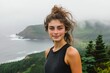 © Shery - A young woman with windblown hair smiles at the camera with a scenic ocean view behind her.
