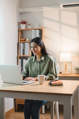 Wall Mural - Young asian woman happily working on laptop in modern home office. The space is well-lit and features stylish decor, creating a productive atmosphere.