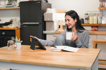 Poster - Woman enjoys a cup of coffee while using a tablet in a cozy home kitchen setting. The relaxed atmosphere encourages productivity and comfort.