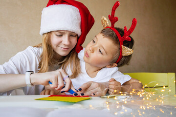 Merry Christmas Happy New Year Teen sister in Santa hat with little boy brother making gifts 