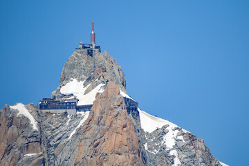 view from below of the station aiguille du midi on the mountain with a clear blue sky and sunshine