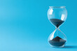 © Aisyaqilumar - A glass hourglass with sand in it is on a blue background. Concept of time passing quickly and the fleeting nature of time