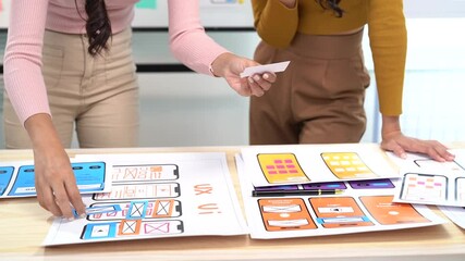 Two female web designers collaborating on a user interface for a mobile phone application. They are reviewing design ideas and discussing the layout