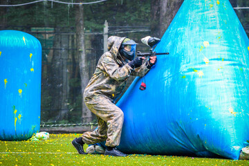 Wall Mural - paintball sport player in protective uniform and mask playing with gun outdoors