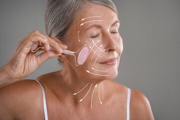 Canvas Print - Beautiful woman doing facial massage with roller on grey background. Arrows on skin showing direction of moves