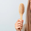 © Neha - A woman's hand holding a hair brush, a few hair strands on a hairbrush, showcasing an issue of hair fall, light background