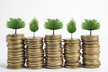 Stacked coins with tiny green trees on white background