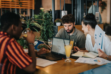 Wall Mural - A diverse group of professionals collaborate in a business meeting at a coffee bar, working with laptops, charts, and drinks. Teamwork and discussion in a casual cafe setting.