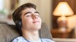 © angel_nt - A young man sitting comfortably on a couch closes his eyes and listens to music through headphones, enjoying a tranquil moment in a homely, well-lit space