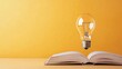 © olegganko - A floating light bulb above an open book against a vibrant yellow background