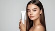 © Danudet.C - An elegant woman with straight hair gracefully holds a luxury cosmetic cream tube, her flawless skin glowing against the pure white background.
