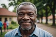 © ThomasLENNE - Close portrait of a smiling senior Nigerian man looking at the camera, Nigerian outdoors blurred background