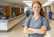 © Rapid Stock - Smiling redhead nurse wearing gray scrubs in a bright and inviting hospital hallway