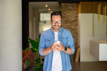 Positive male manager in glasses checking social media applications over mobile phone in modern office