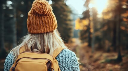 An adventurous traveler wearing an orange beanie and sporting a yellow backpack explores a forest trail during autumn, capturing the allure and excitement of an outdoor journey in nature.