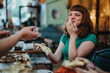 © qunica.com - A cheerful young woman laughs while sharing pizza with friends in a cozy, vibrant cafe setting. The atmosphere is lively and relaxed, capturing the joy of casual dining and socializing.