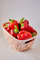 textured beige basket filled with red sweet bell peppers on light background close-up, healthy eating concept