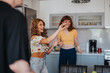 © qunica.com - Two young women happily socializing in a kitchen environment, enjoying each other's company and creating joyful memories. A scene filled with laughter and friendship.