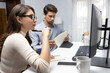 © InfiniteFlow - Concentrating beautiful woman holding pen analyzing while looking computer to search financial information data report next to smart coworker catching note at modern office in morning time. Postulate.