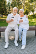 © dikushin - Full length vertical portrait of loving senior couple enjoying coffee sitting hugging on park bench, basking in summer warmth, exuding love and happiness, embodying love and happiness in retirement.