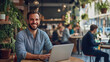 © Michael - Young freelancer happily working on his laptop in a bustling coffee shop filled with busy individuals