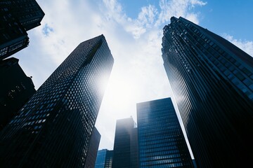 Cinematic skyscape-style view of tall buildings in a city under daylight, featuring sunlight, shadows, and blue sky, ideal for business backgrounds.