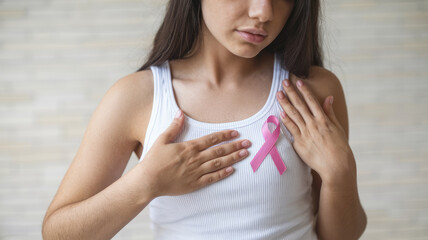 A woman wearing a white tank top with a pink ribbon on it. She is holding her chest