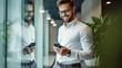 © halo - A handsome businessman stands in front of the glass wall, smiling and looking at his phone while standing inside an office with modern decor.