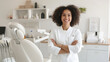 © VERTEX SPACE - A smiling woman in dental clinic, wearing white coat, stands confidently with her arms crossed. bright, modern environment reflects welcoming atmosphere for patients